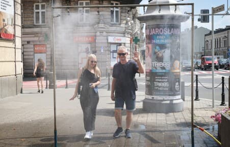 Kurtyna wodna na chodniku przy ul. Jana Pawła II. Dwoje przechodniów korzystających z kurtyny. Miasto